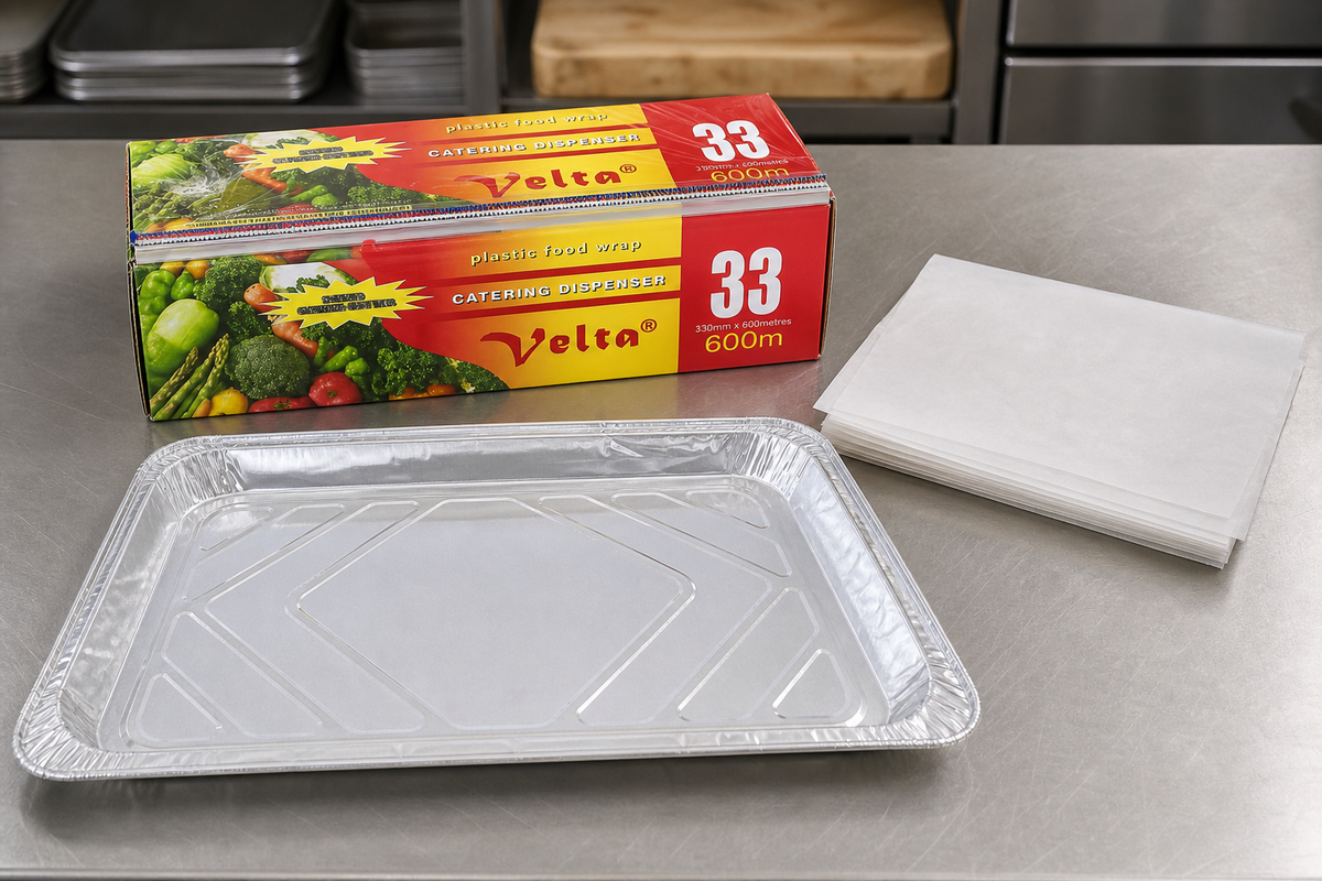 Aluminium foil catering trays beside a commercial cling wrap dispenser roll and greaseproof deli sheets
